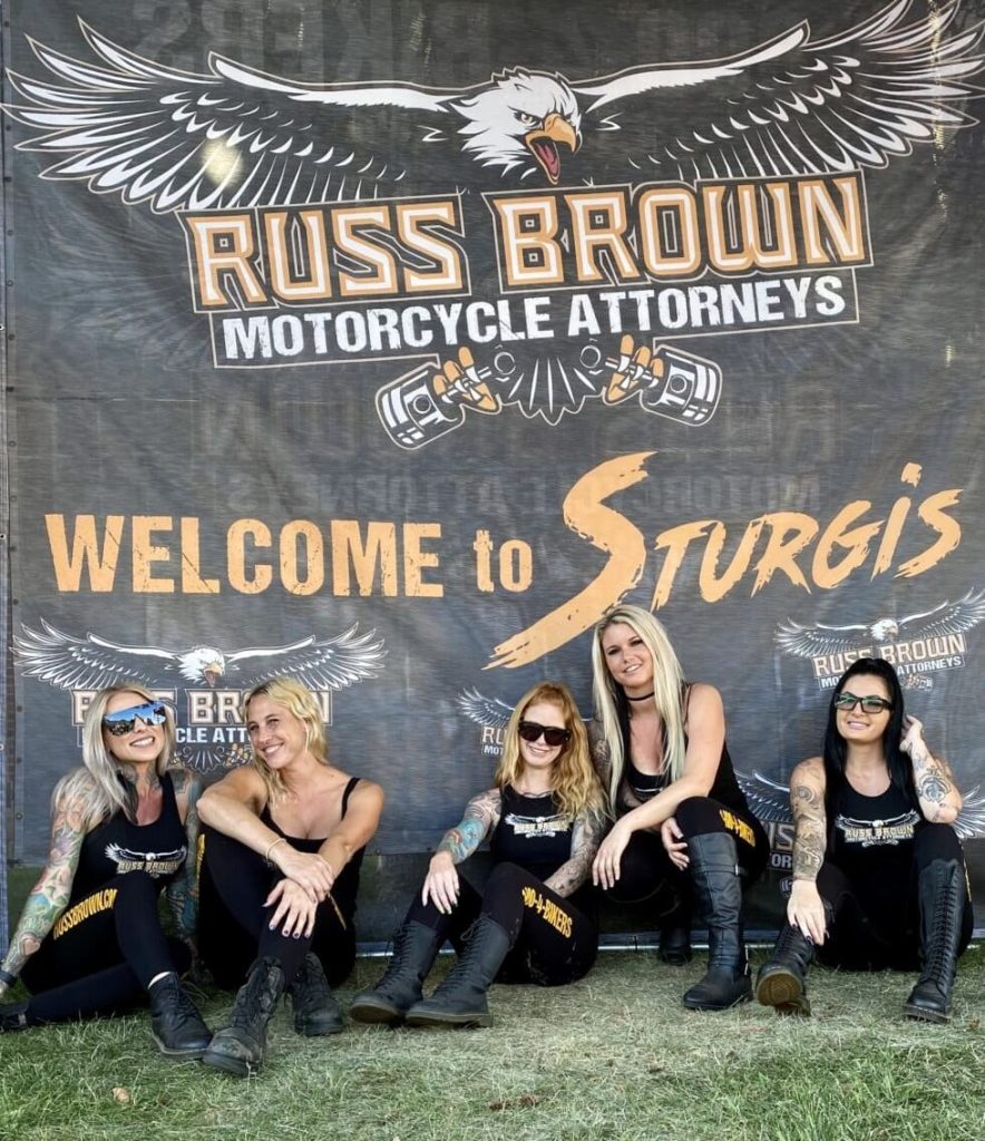 Girls Sitting Down By RBMA Welcome To Sturgis Sign